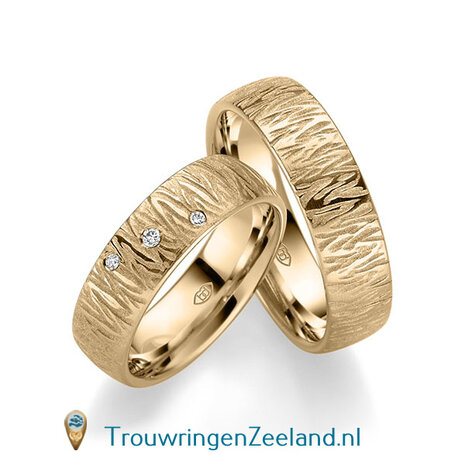Trouwringen in 14/18 karaat witgoud mat en glans 6,0 mm. breed met golven overdwars en in de damesring 3 diamanten schuin gezet per paar vanaf