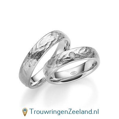 Trouwringen in 14/18 karaat witgoud bewerkt 5 mm. breed met in de damesring 1 diamant